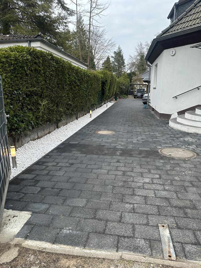 Gepflasterte Einfahrt mit Hecke, Zierkiesstreifen und Bodenleuchten