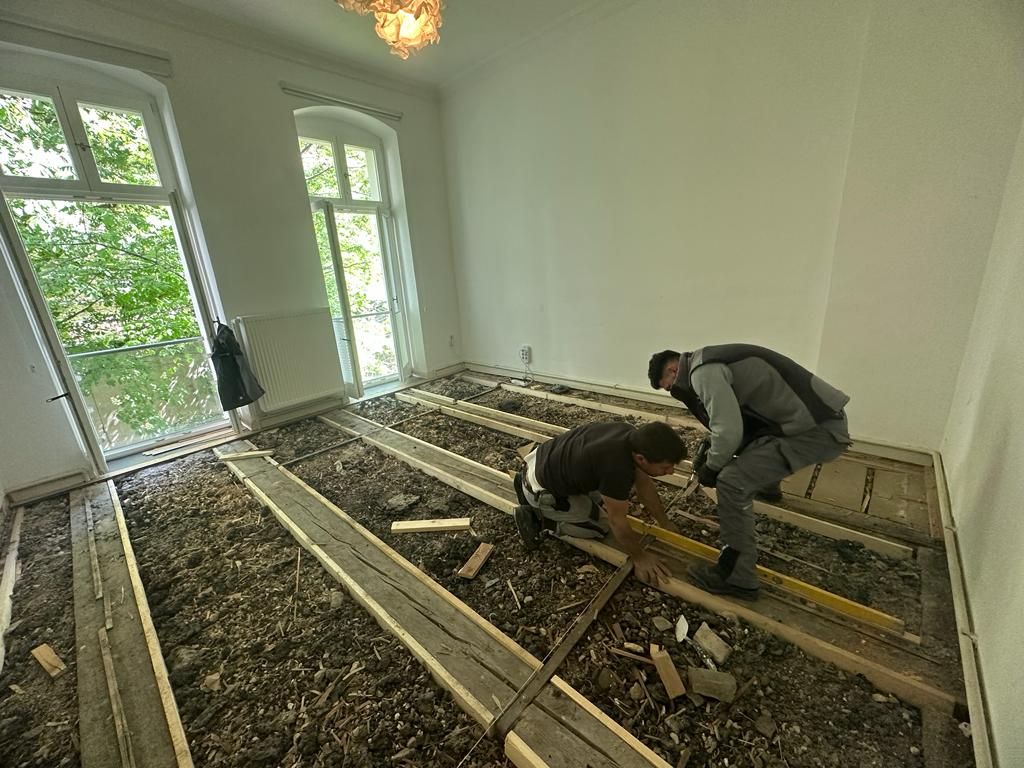 Zwei Mitarbeiter von Falax-Bau richten neue Lagerhölzer im Dielenboden aus